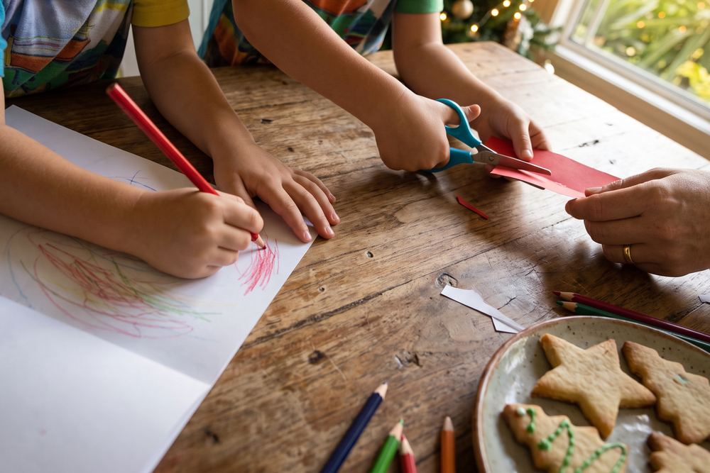 Mãos de crianças colorindo e recortando atividades de Natal